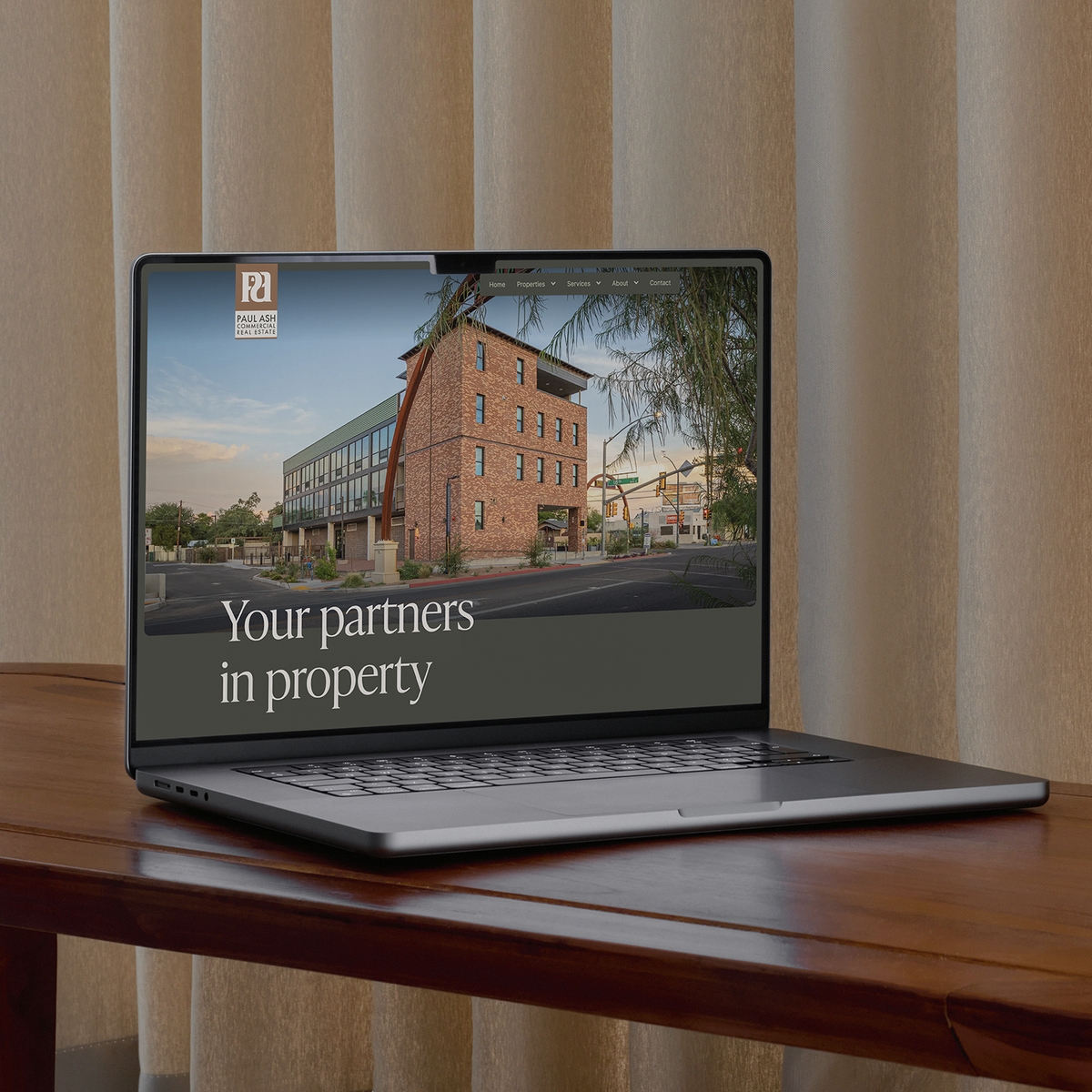 Paul Ash CRE website homepage displyed on a MacBook laptop that is sat on a polished wooden side table.